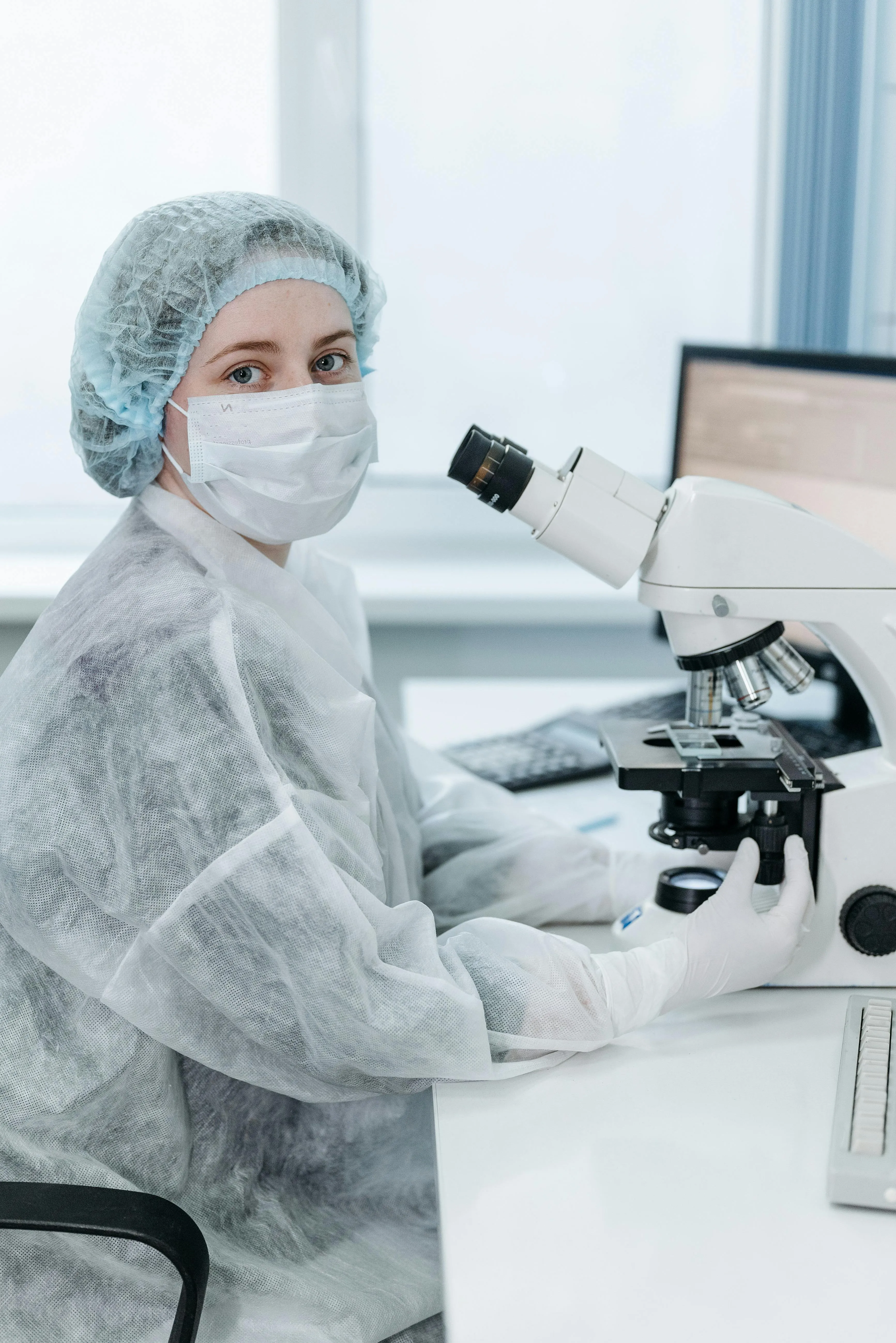 A woman wearing protective gear in a laboratory, working with a microscope and test tubes